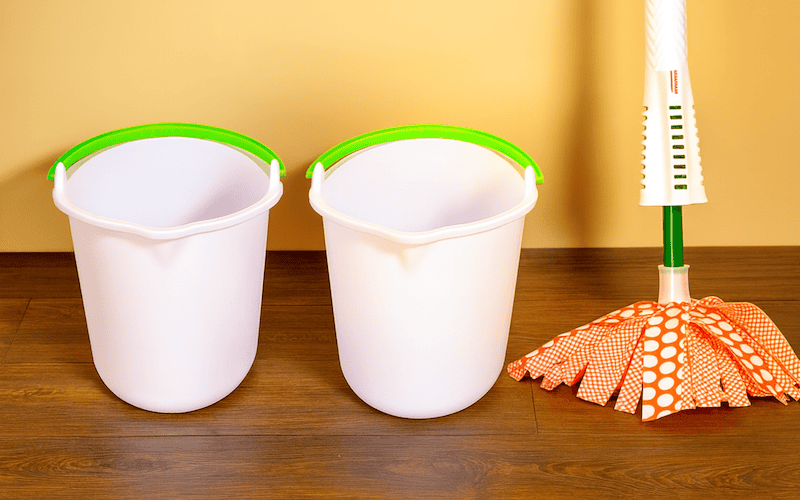 Microfiber mop and warm water bucket placed on a laminate floor for gentle cleaning.