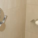 Close-up of shower tiles and chrome fixtures with visible water spots and soap residue, illustrating the need for no-scrub tile cleaning methods.