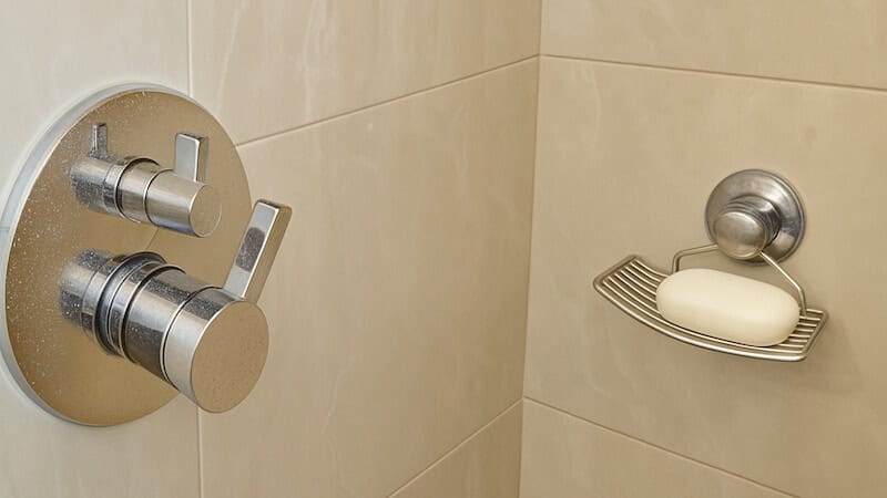 Close-up of shower tiles and chrome fixtures with visible water spots and soap residue, illustrating the need for no-scrub tile cleaning methods.